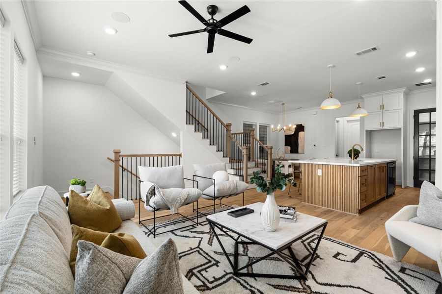 Spacious, open-concept living area is well-lit with natural light and has a cozy seating area with stylish decor and a contemporary staircase leading to the upper floor.