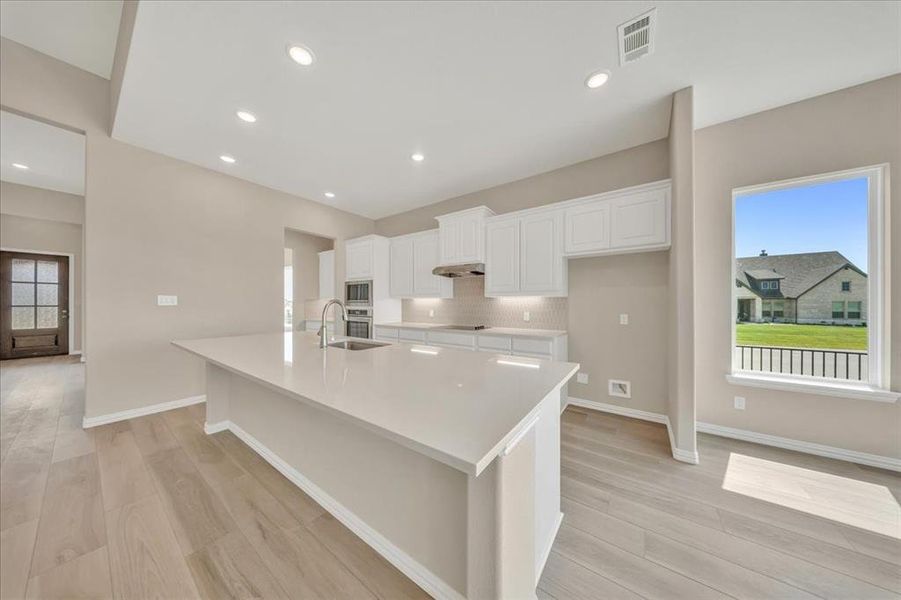 Kitchen with appliances with stainless steel finishes, white cabinets, light wood-style flooring, a spacious island, and recessed lighting Kitchen with appliances with stainless steel finishes, white cabinets, light wood-style flooring, a spacious island, and recessed lighting