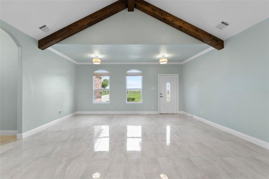 Empty room featuring light tile patterned floors and vaulted ceiling with beams