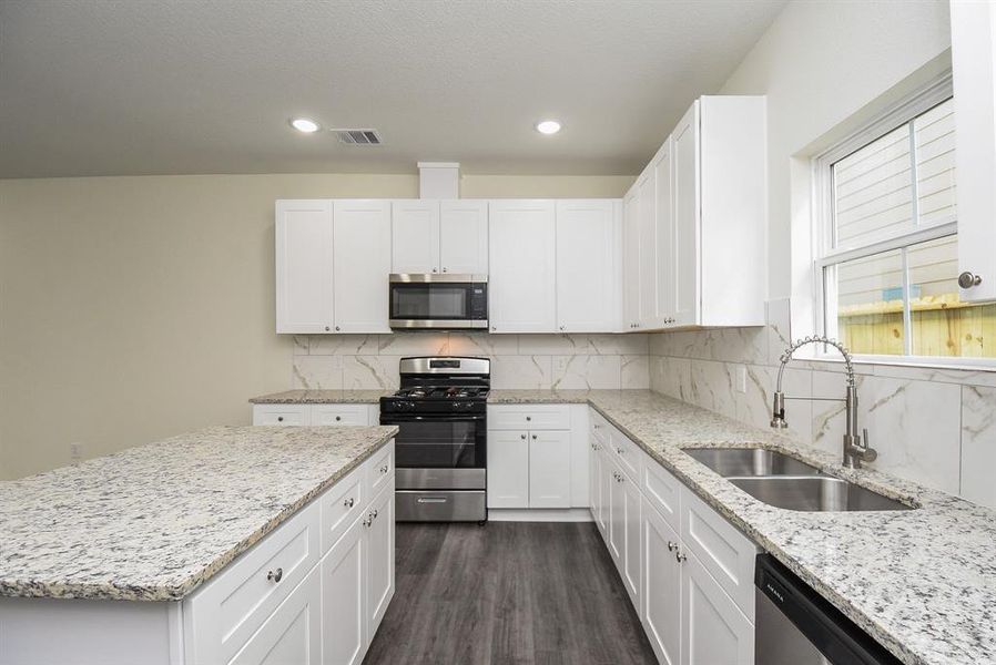 A modern kitchen with white cabinetry, stainless steel appliances, granite countertops, and a window over the sink.