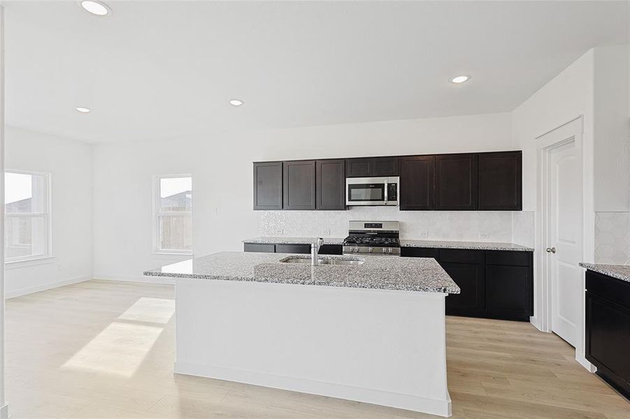 Kitchen featuring a center island with sink, sink, light stone countertops, appliances with stainless steel finishes, and light hardwood / wood-style floors