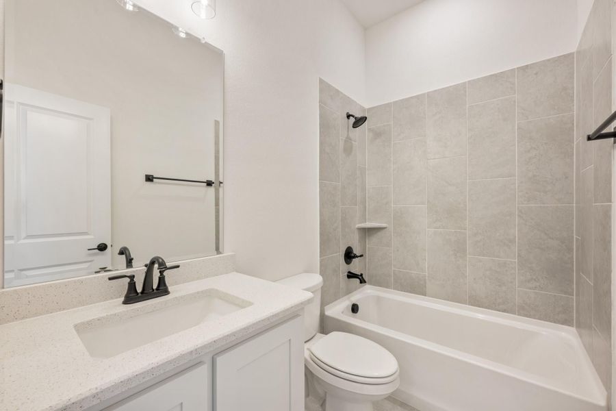 Bathroom with white quartz vanity, toilet, and tub-shower combo with gray tile surround and dark bronze fixtures Bathroom with white quartz vanity, toilet, and tub-shower combo with gray tile surround and dark bronze fixtures
