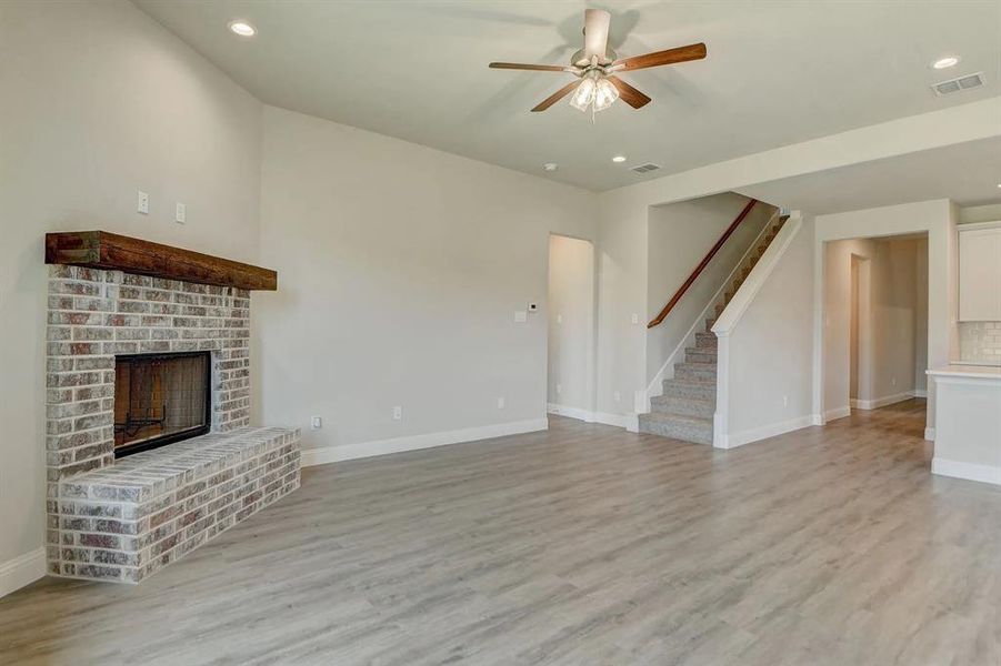 Unfurnished living room featuring a fireplace, stairway, a ceiling fan, light wood-style flooring, and baseboards