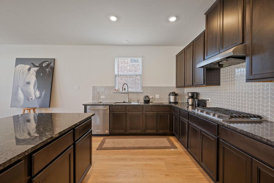 Kitchen with dark wood finish cabinetry, dark stone countertops, light wood-style floors, stainless steel appliances, and recessed lighting