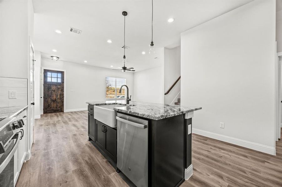 Kitchen with stainless steel appliances, a center island with sink, hardwood / wood-style floors, sink, and decorative light fixtures