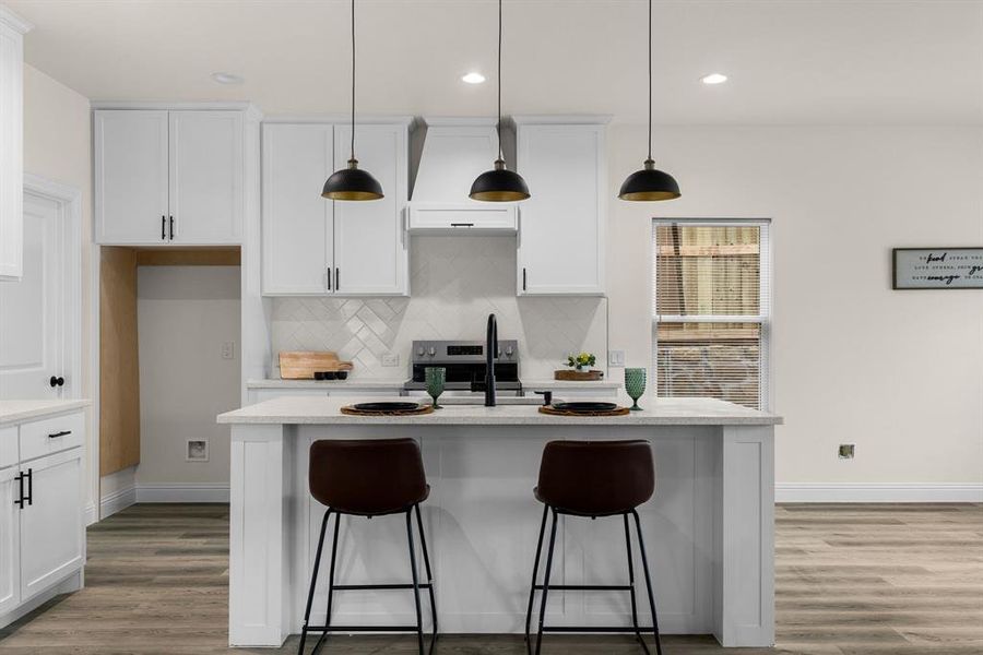 Kitchen featuring hanging light fixtures, white cabinetry, and a kitchen island with sink