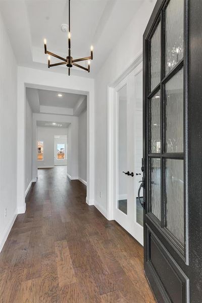 Hallway featuring dark wood-type flooring, a raised ceiling, and a notable chandelier