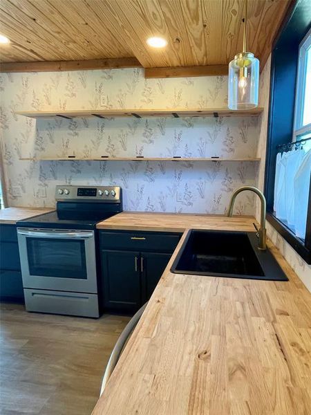Kitchen featuring stainless steel electric stove, wood butcher block counters, and open shelves