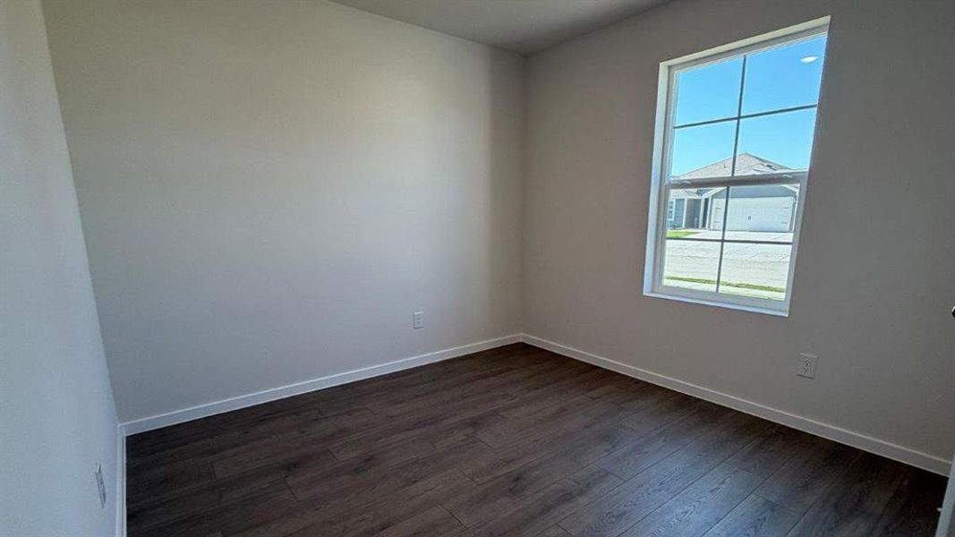 Bright room featuring wood-finish flooring, white baseboards, light neutral wall paint, and a window with white framing Bright room featuring wood-finish flooring, white baseboards, light neutral wall paint, and a window with white framing