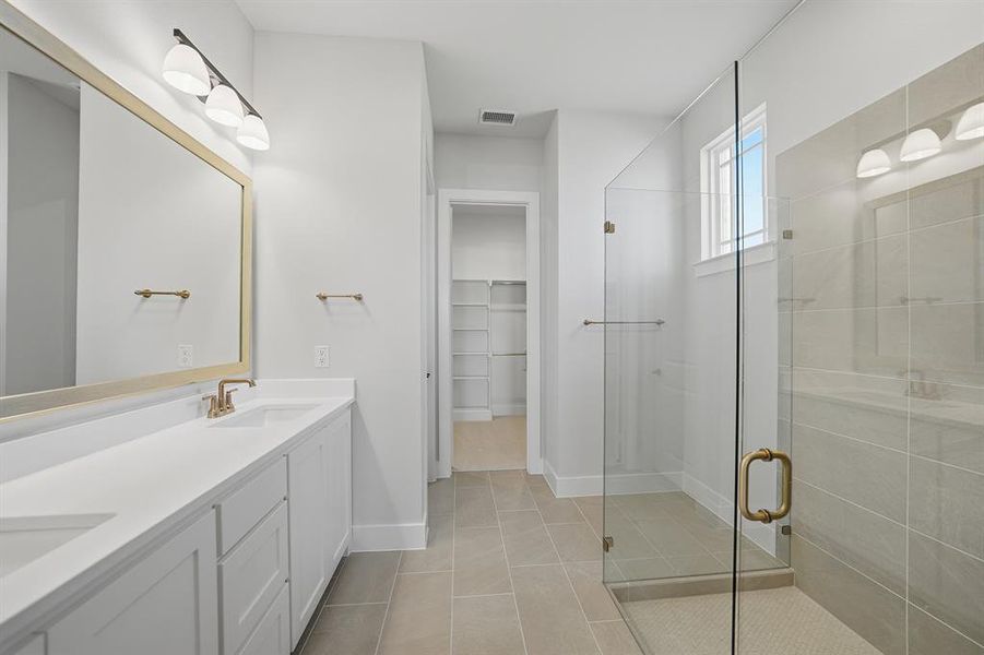 Full bath with a walk in closet, double vanity, a stall shower, and light tile patterned floors