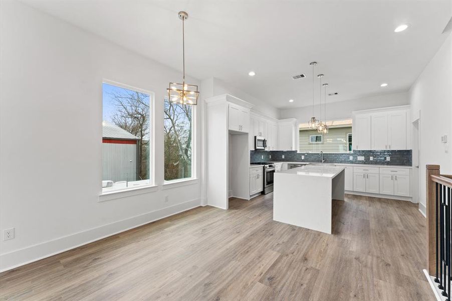 This modern kitchen features sleek white cabinetry, a spacious island, and stainless steel appliances. The open layout is complemented by large windows that bring in plenty of natural light, enhancing the bright and airy feel. The wood flooring adds warmth to the contemporary design.