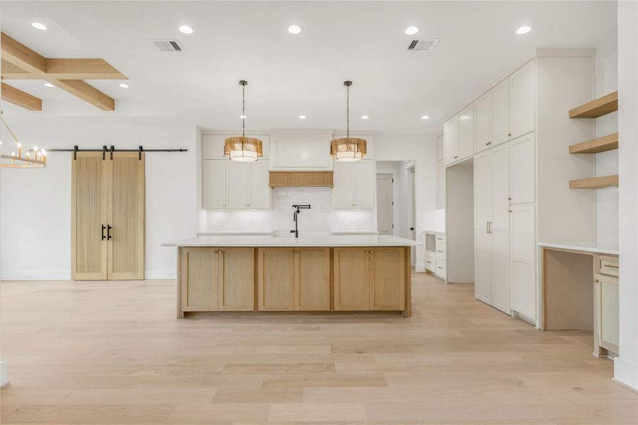 Kitchen with a barn door, an island with sink, light wood-style floors, decorative light fixtures, and beamed ceiling