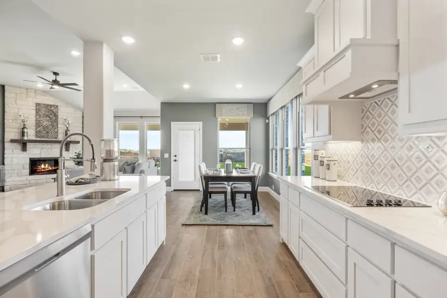 Open kitchen with white cabinets, quartz countertops, and patterned tile backsplash, open to dining area and living room with fireplace.