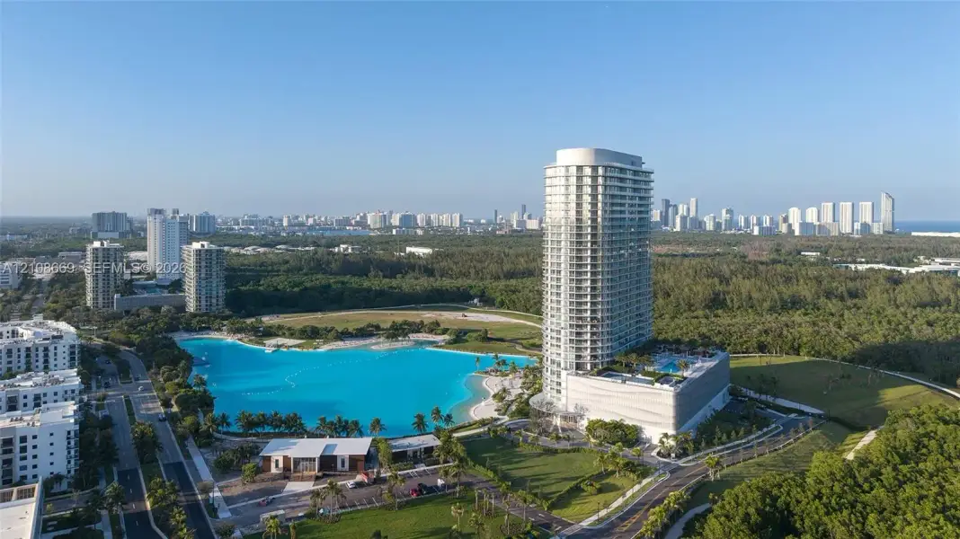 High-rise residential tower featuring a multi-story parking structure, private outdoor swimming pool, and proximity to a large-scale recreational lagoon