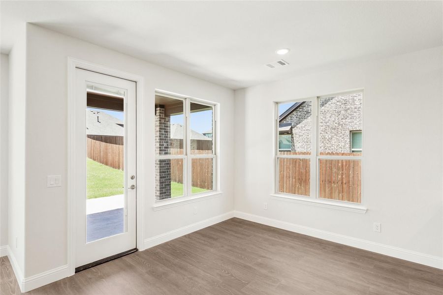 Empty room with wood-look floors, white walls, back door, and large windows overlooking fenced backyard