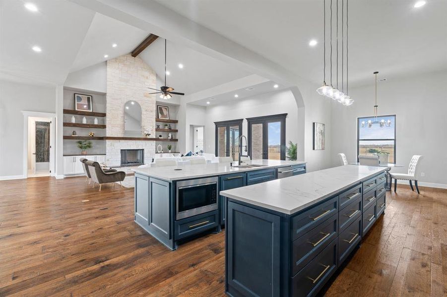 Kitchen featuring a center island with sink, beamed ceiling, stainless steel microwave, sink, and decorative light fixtures