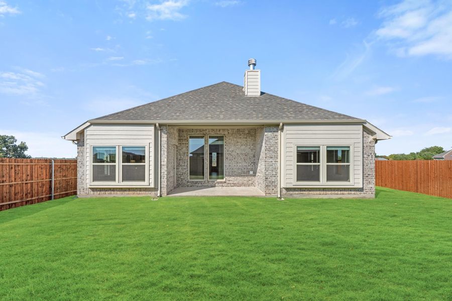 Rear exterior of single-story brick home with covered patio, large green lawn, and wood privacy fence.