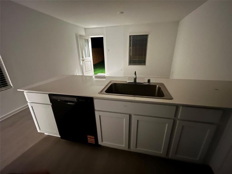 Kitchen island with white cabinetry, a stainless steel sink, and a black dishwasher Kitchen island with white cabinetry, a stainless steel sink, and a black dishwasher
