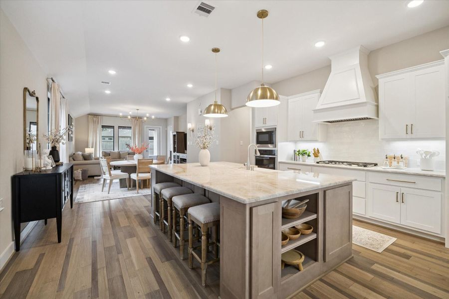 The kitchen features an over-sized Taj Mahal Quartzite island, 36" 5 burner cook-top, drawer/cabinet pulls, pendant lighting in bronze finishes, built in microwave, and oven.