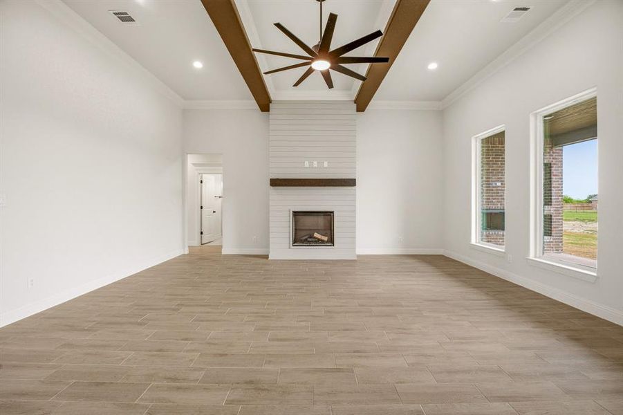 Unfurnished living room with ceiling fan, a large fireplace, wood tiled floors, crown molding, and beam ceiling