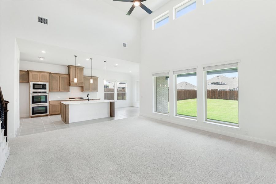 Open-concept living room with high ceilings and ceiling fan, flowing into kitchen with wood cabinets and center island