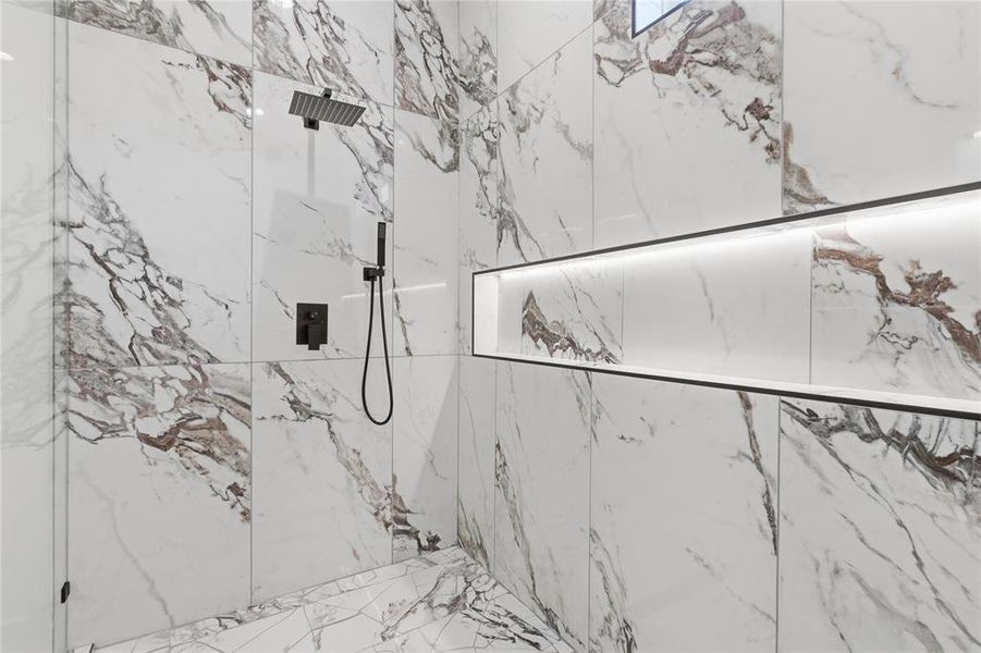 Spacious shower featuring floor-to-ceiling veined white and brown tile, a rain shower head, a handheld shower fixture, a built-in recessed shelf with integrated lighting, and a glass enclosure Spacious shower featuring floor-to-ceiling veined white and brown tile, a rain shower head, a handheld shower fixture, a built-in recessed shelf with integrated lighting, and a glass enclosure