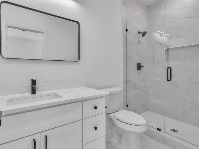 Bathroom featuring a marble finish shower, vanity, and toilet Bathroom featuring a marble finish shower, vanity, and toilet