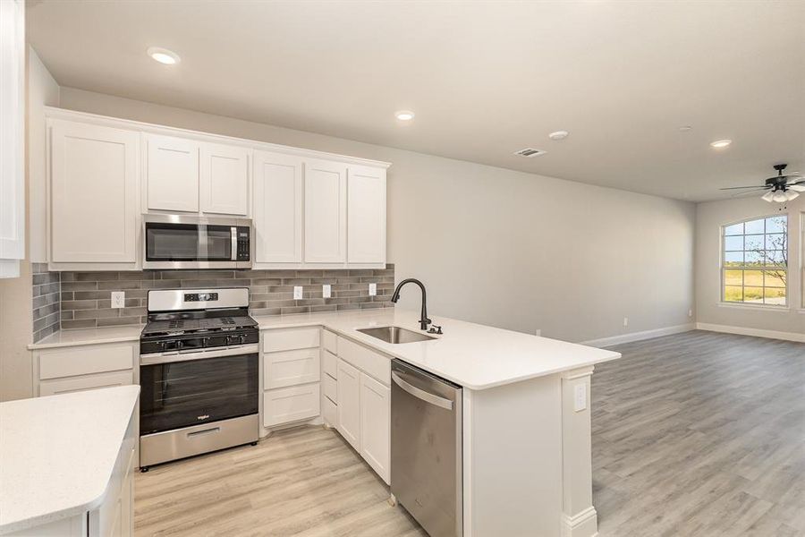 Kitchen featuring light hardwood / wood-style floors, kitchen peninsula, white cabinets, and stainless steel appliances