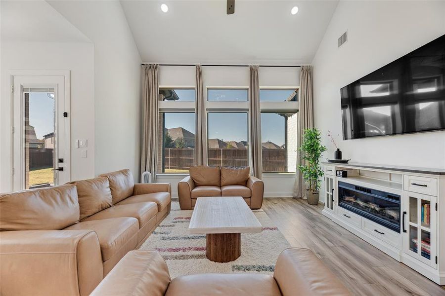 Living room featuring light wood-style flooring, vaulted ceiling, recessed lighting, and a glass covered fireplace