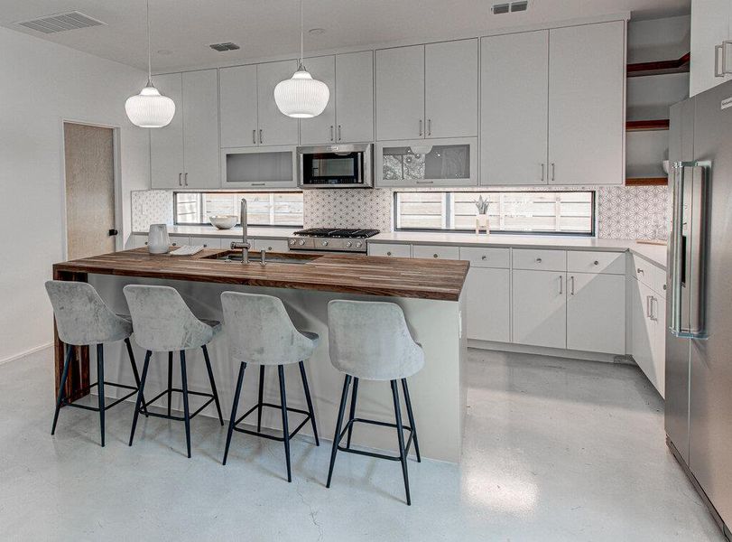 Kitchen with butcher block counters, a sink, visible vents, finished concrete flooring, and appliances with stainless steel finishes