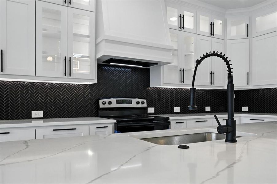 Kitchen with range with electric cooktop, custom exhaust hood, white cabinetry, and glass insert cabinets