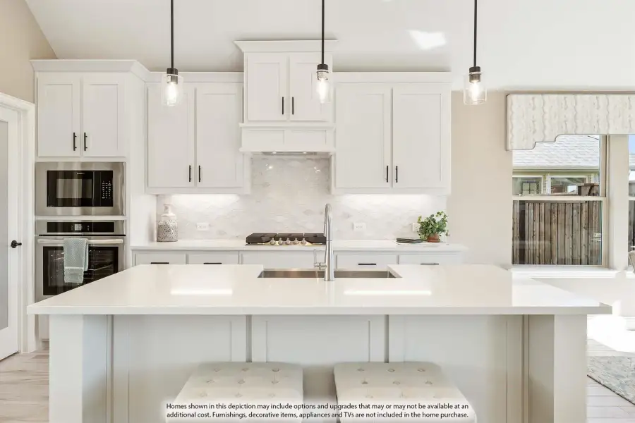 White kitchen with large island, pendant lights, tile backsplash, and stainless steel appliances