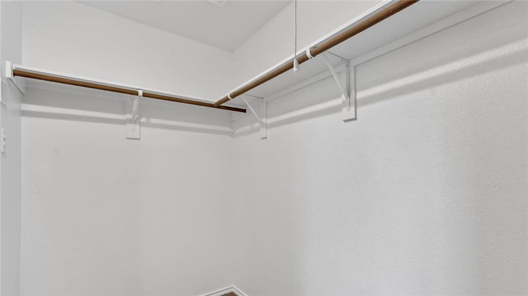 Walk-in closet featuring white painted walls, wood-finish hanging rods, and white shelf supports Walk-in closet featuring white painted walls, wood-finish hanging rods, and white shelf supports