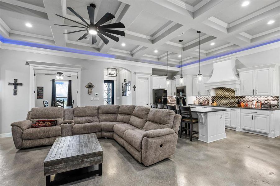 Living room with coffered ceiling, beam ceiling, crown molding, and ceiling fan