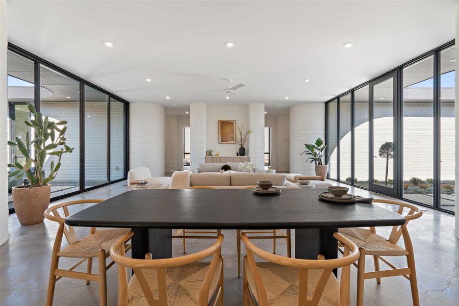 Dining area featuring ceiling fan, a wall of windows, and concrete floors