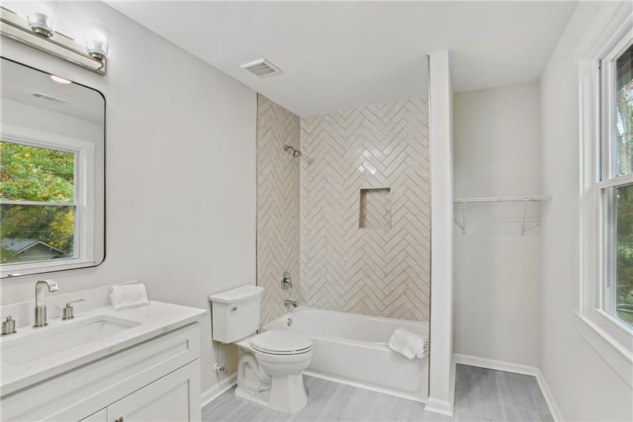 Full bathroom with tiled shower / bath combo, toilet, and large vanity