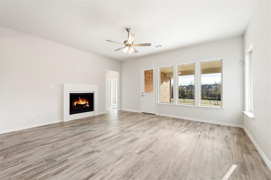 Unfurnished living room featuring light wood-style flooring, a warm lit fireplace, and ceiling fan