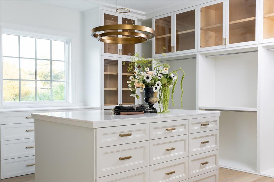 A primary closet with bespoke built-ins, elegant bronze hardware, and a spacious packing island for ultimate organization A primary closet with bespoke built-ins, elegant bronze hardware, and a spacious packing island for ultimate organization
