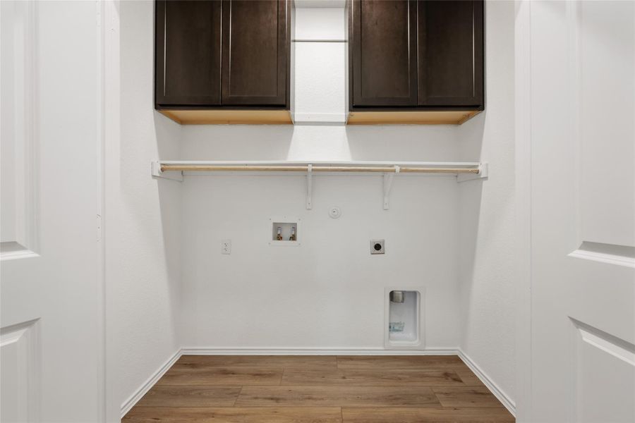 Laundry area featuring cabinet space, hookup for an electric dryer, light wood-style floors, and gas dryer hookup Laundry area featuring cabinet space, hookup for an electric dryer, light wood-style floors, and gas dryer hookup
