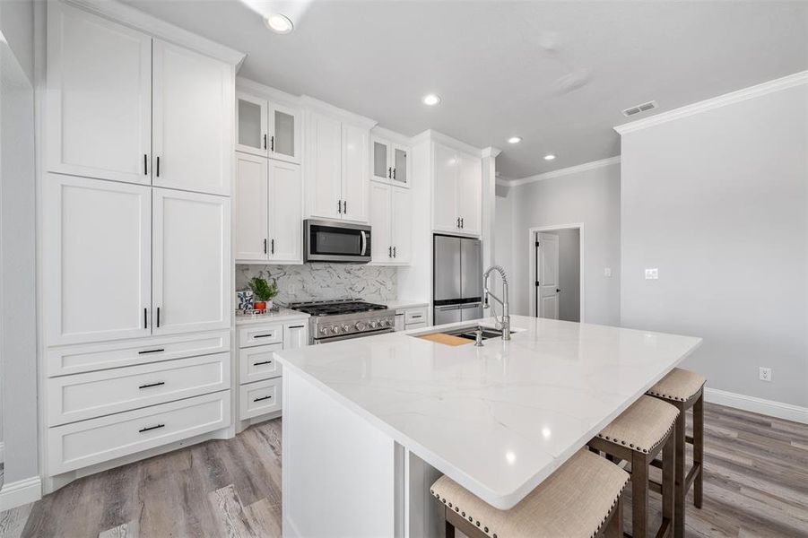 Kitchen featuring light stone countertops, an island with sink, appliances with stainless steel finishes, and a kitchen bar