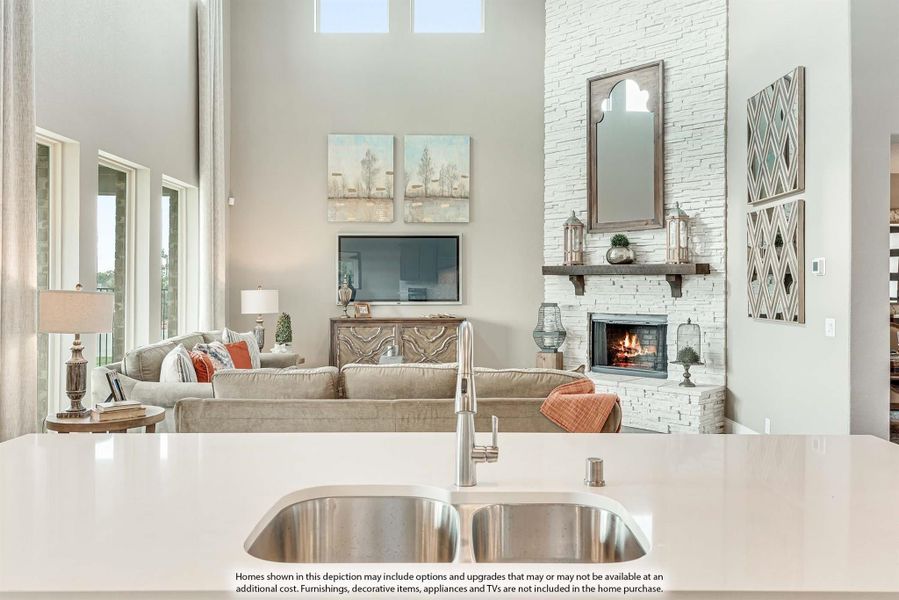 Open-concept living area with white stone fireplace, high ceilings, and kitchen island with stainless steel sink in foreground