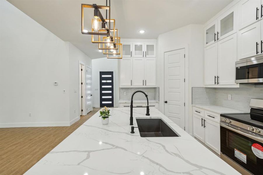 Kitchen with stainless steel appliances, light hardwood / wood-style floors, tasteful backsplash, and decorative light fixtures