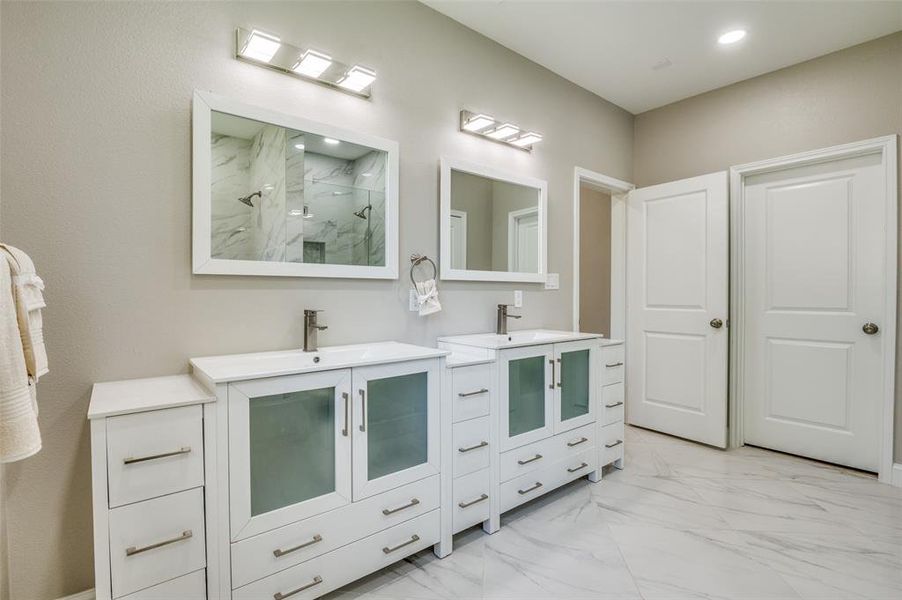 Bathroom featuring light marble finish flooring, two vanities, and a marble finish shower
