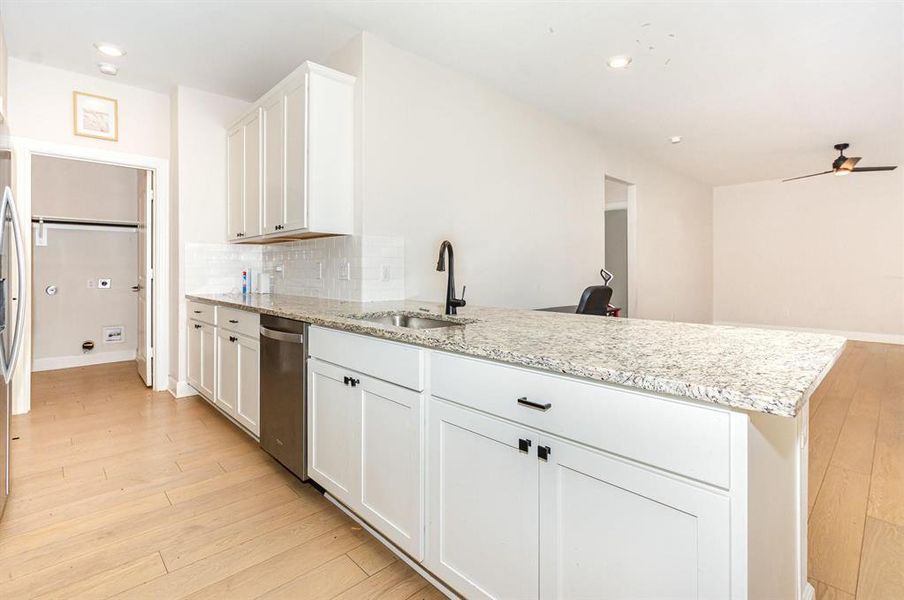 Kitchen featuring white cabinets, decorative backsplash, light stone counters, light wood-type flooring, and dishwasher Kitchen featuring white cabinets, decorative backsplash, light stone counters, light wood-type flooring, and dishwasher