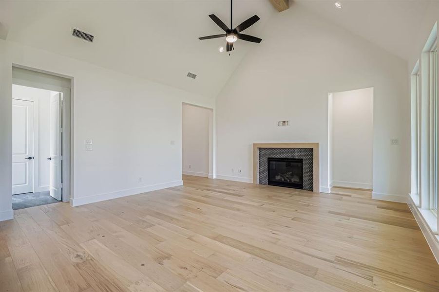 Unfurnished living room featuring beamed ceiling, light wood-style flooring, a ceiling fan, high vaulted ceiling, and a tiled fireplace