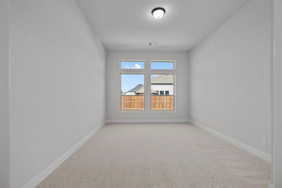 Bright room featuring a series of rectangular windows, neutral-toned carpeting, white baseboards, light grey wall paint, and a ceiling-mounted light fixture Bright room featuring a series of rectangular windows, neutral-toned carpeting, white baseboards, light grey wall paint, and a ceiling-mounted light fixture
