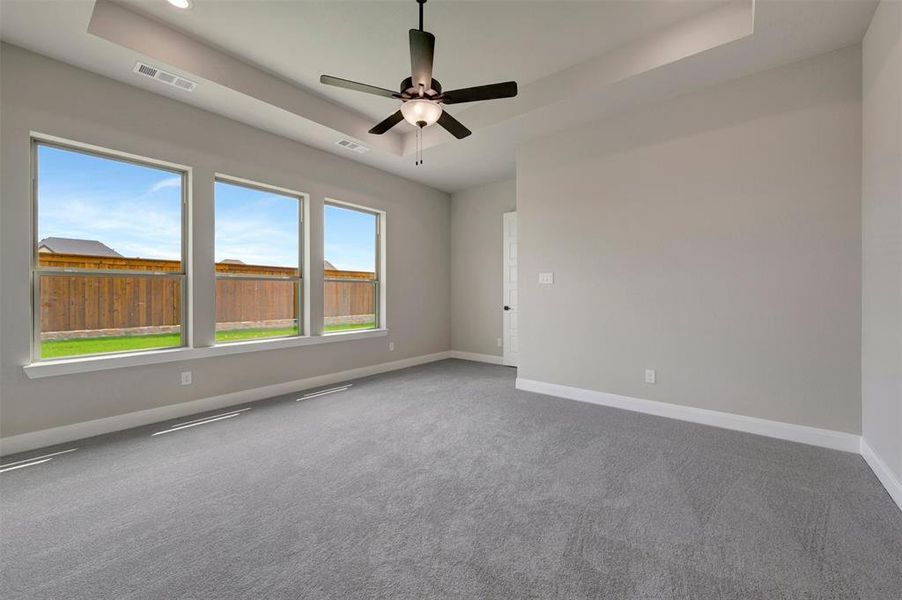 Spacious room featuring three large windows, tray ceiling with recessed lighting, and a dark-toned ceiling fan