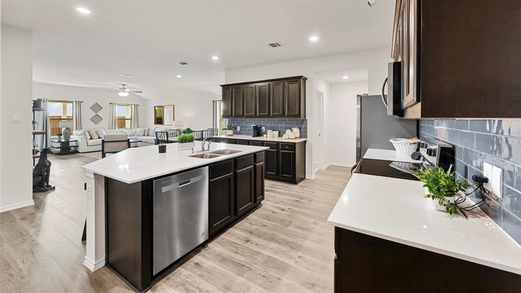 The kitchen features dark wood cabinetry, white countertops, a stainless steel dishwasher, and a blue tile backsplash