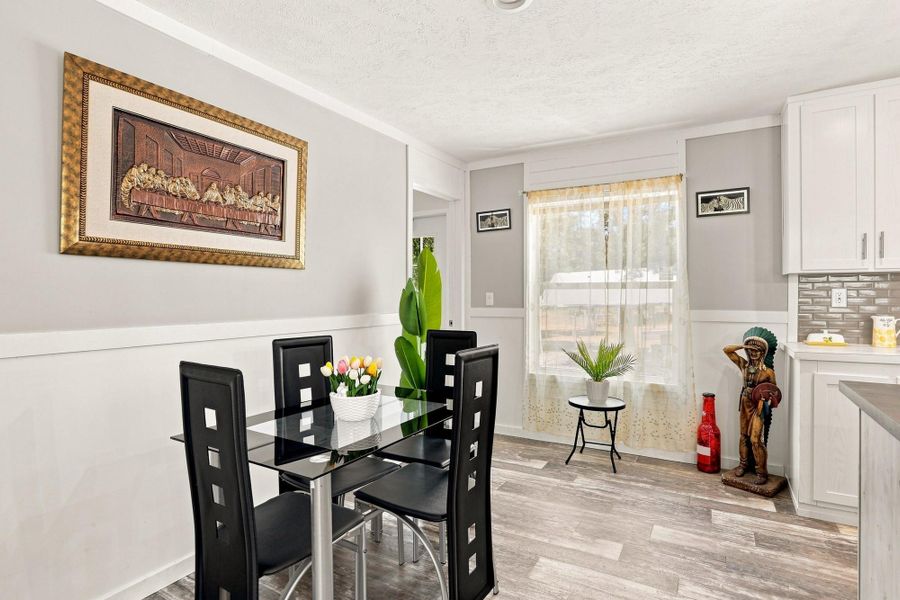 An inviting dining space boasts wood-look flooring and wainscot paneling next to the kitchen.