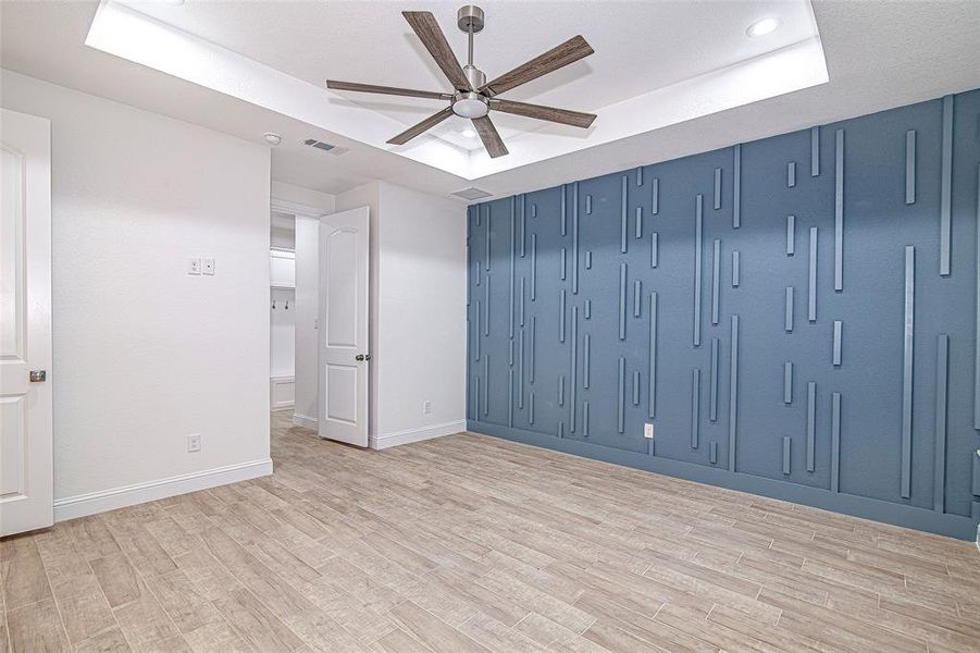 Empty room with a tray ceiling, a ceiling fan, light wood-style floors, baseboards, and recessed lighting Empty room with a tray ceiling, a ceiling fan, light wood-style floors, baseboards, and recessed lighting